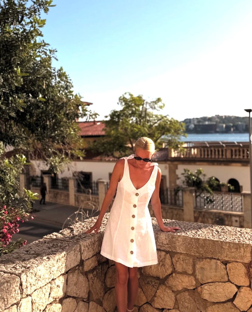 Alena Kulikova on a stone terrace overlooking a Mediterranean town
